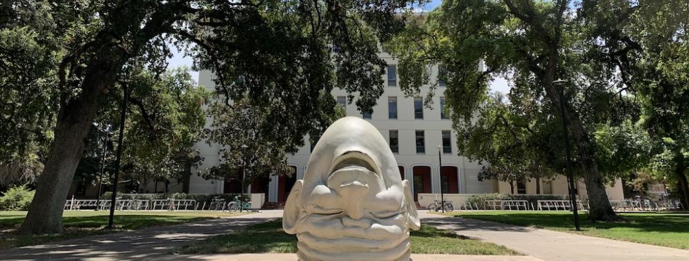 Eye on Mrak (Fatal Laff): A UC Davis Egghead — The upside-down head points away from the administration building, laughing. On the back of the head, a single eye stares at Mrak Hall.