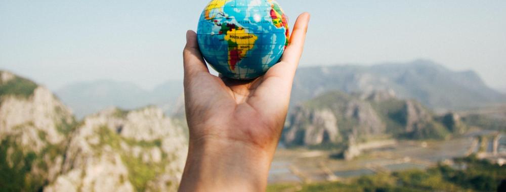 A globe held in the palm of a hand, with a landscape in the background.